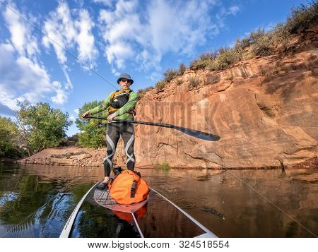 senior man paddling a stand up paddleboard  a mountain lake with sandstone cliffs - Horsetooth Reservoir , COlorado, in early fall scenery
