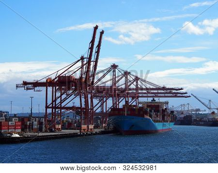 Seattle, Wa - May 18, 2019:  Shipping Boat Unloaded In Seattle Harbor By Red Cranes During The Day.