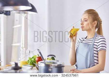 The Girl At The Table In The Kitchen With A Glass Of Orange Jui