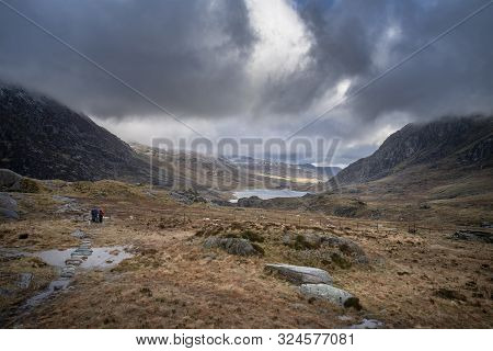 Hikers In Ogwen Valley Winter Landscape With Snowcapped Pen Yr Ole Wen And Tryfan Mountains With Dra