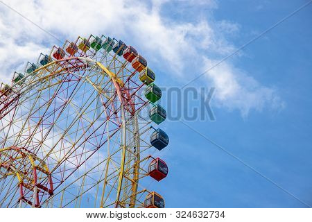 Ferris Wheel On Blue Sky Background. Ferris Wheel Attraction In Summer Park. Orange Metallic Constru