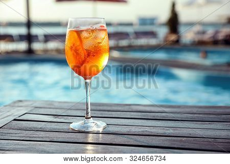 Glass Of Fresh Summer Cocktail On Wooden Table Near Swimming Pool Outdoors. Space For Text