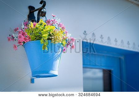 Bink Flowers In A Blue Bucket Hung On A White Wall In A Traditional Fishing Village Of The Mediterra