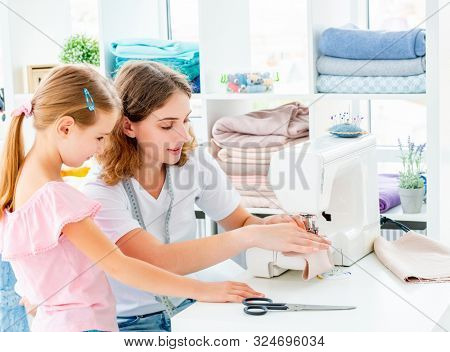 Little girl is taught to sew by teacher at class
