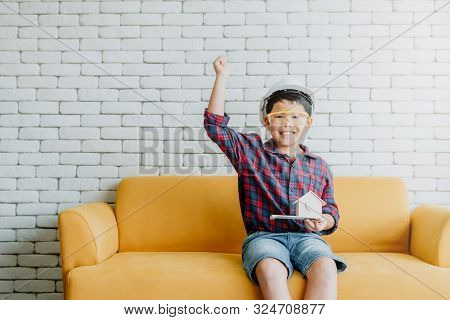 Happy Asian Child Boy With Safety Hat Inspires To Be Engineer For His Future Career Holding House Mo