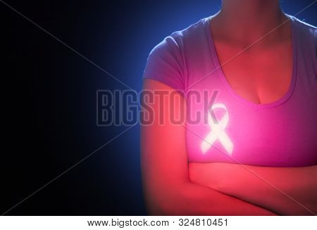 Woman on dark background. Luminescent pink ribbon like a symbol of breast cancer awareness. Support people living with tumor illness.