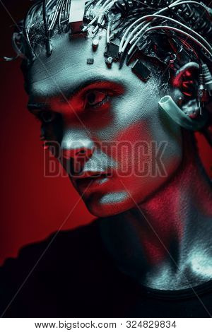 Portrait of a cyborg looking up over red background. Biological human robot with wires implanted in the head. Technologies of the future.