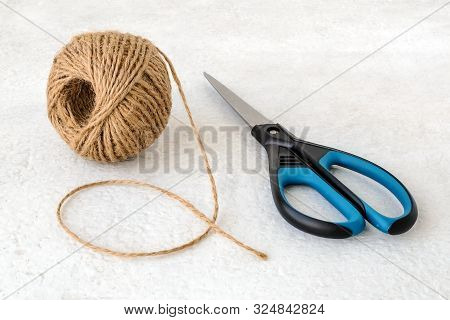 Natural Hemp Cord Ball And Scissors On A Rough White Surface. Roll Of Jute String Or Flax Twine. Coa