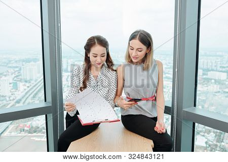 Young Vietnamese Businesswoman Discussing Chart In Financial Report With Coworker When Thay Are Sitt