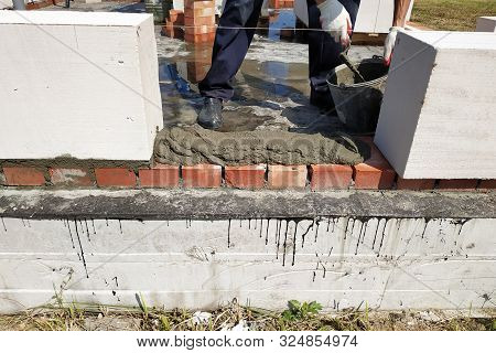 The Worker Begins The First Row Of Masonry Construction In White Gas Blocks.