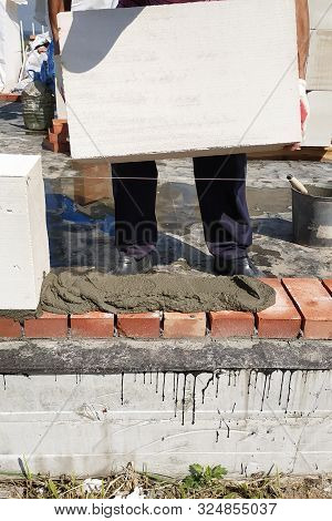 The Worker Begins The First Row Of Masonry Construction In White Gas Blocks.