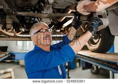 Senior grey-haired technician of repair service with worktool fixing details of car while repairing it