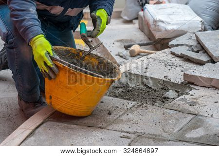 A Worker Strengthens The Stones Of The Street With Trowel, Sand And Concrete. Indursty.