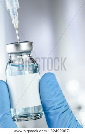Healthcare concept with a hand in blue medical gloves holding a vaccine vial with blue liquid and black white label