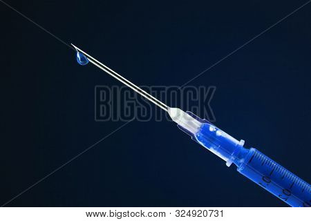 Syringe filled with blue drug and dripping from the needle