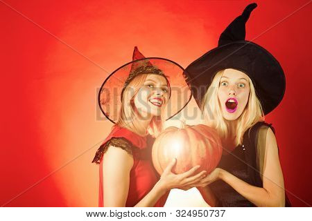 Two Emotional Young Women In Halloween Costumes On Party Over Orange Background With Pumpkin.