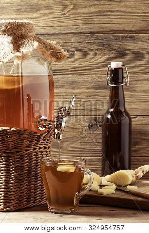 Fresh Homemade Kombucha Fermented Tea Drink In Jar With Faucet And In Cup And Bottle On Wooden Backg