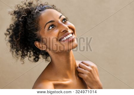 Beautiful african woman laughing and looking up in joy. Portrait of cheerful young woman with bare shoulders isolated on background. Beauty afro american girl with curly hair smiling.