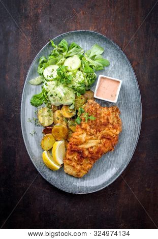 Fried Wiener schnitzel from veal topside with fried potatoes and lettuce as top viewon a modern design plate with copy space