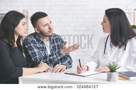 Young Childless Couple Consulting With Doctor At Clinic, Discussing Treatment Plan, Free Space