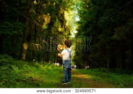 Cute Little Blond Boy With A Toy In The Forest Road.
