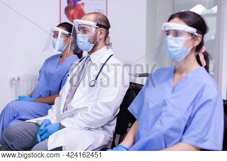 Worried Mature Doctor Sitting In Waiting Room Of Hospital Clinic With Medical Nurse Team Looking At 
