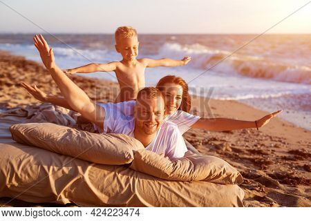 Dad Tosses His Son Up. Lie On A Bed By The Sea At Sunset. Family Vacation On The Sandy Beach. Young 
