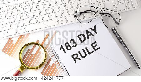 183 Day Rule Text Written On Notebook With Keyboard, Chart,and Glasses