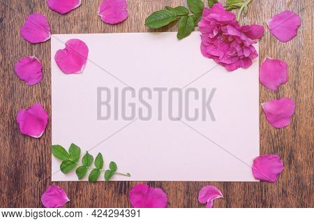 Sheet Of White Paper With Rosehip Flower And Its Petals On A Wooden Table