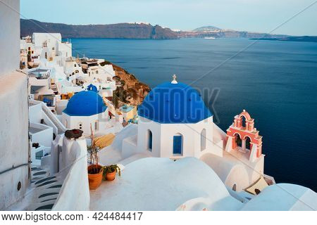 Famous view from viewpoint of Santorini Oia village with blue dome of whitewashed greek orthodox Christian church of traditional greek architecture. Oia town, Santorini island, Greece