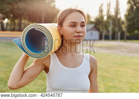 Young Attractive Female With Dark Hair Wearing White Top Standing Outdoor In Stadium And Holding Kar