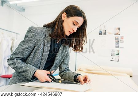 Side View Of A Seamstess Female Cutting With Scissors The Fabrics. Business Owner Woman Working On A