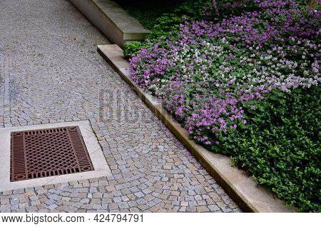 Shady Corner Behind The House By A Road Of Granite Cubes. Metal Ventilation Grilles In The Tiles Res