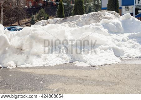 A Large Melting Pile Of Snow On The Dried Asphalt In The Spring. It's The Snow That's Being Taken Ou
