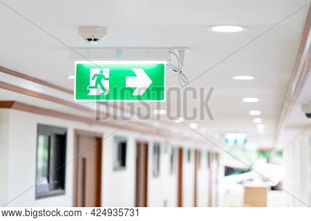 A Arrow Light Box Sign Of Emergency Fire Exit Is Hung On The Ceiling In Hospital Walkway, Idea For E