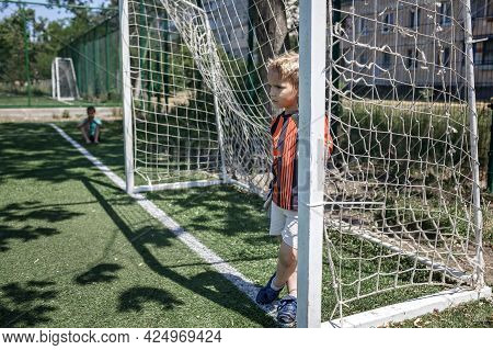 Little Boy In Black And Orange Form Playing Football On Open Field In The Yard, A Young Soccer Playe