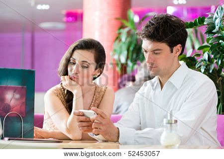 Couple in a cafe spends leisure time together, she is angry because he is busy on the phone