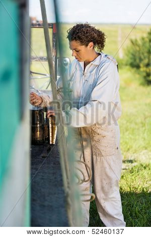 Young female beekeeper preparing smoker for removing honey from hives on truck