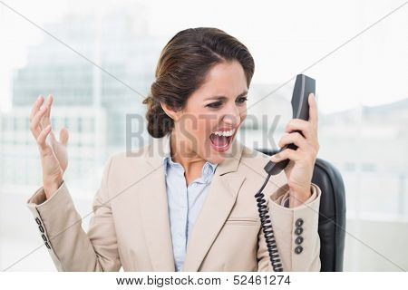 Outraged businesswoman shouting at phone in bright office