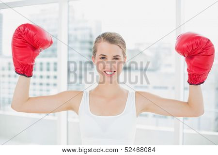 Cheerful competitive woman with red boxing gloves cheering up in bright sports hall