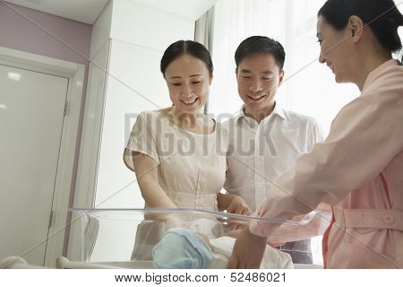 Young happy family with nurse looking down at their newborn 