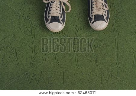 Black sneakers on a green welcome mat