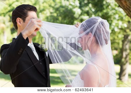 Young loving groom unveiling bride in garden