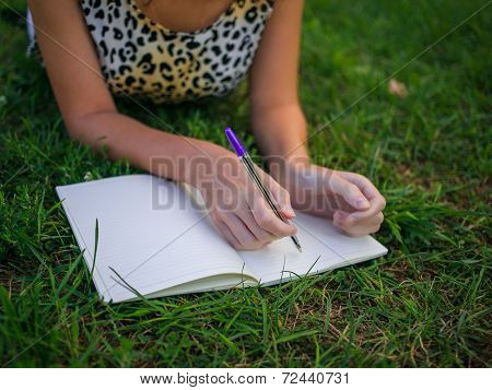 Girl writing something and lying on grass in the summer park