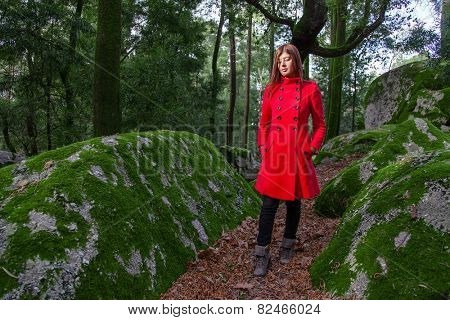 Young woman feeling sad walking on a forest wearing a red overcoat during winter under a sunlight ray