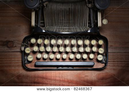 High angle shot of an antique typewriter on a rustic wood table. Closeup on the keys showing only part of the machine. Horizontal format with spot lighting. 