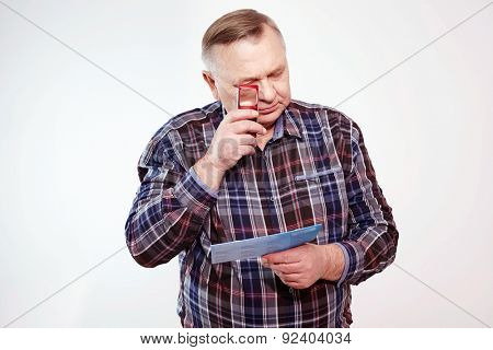 Senior man in plaid shirt reading letter with magnifying glass over white background