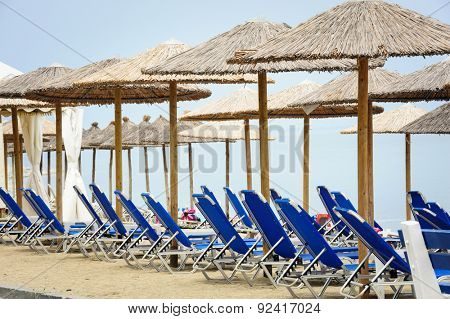 Rows of reed umbrellas and blue deck chair on the sea beach 