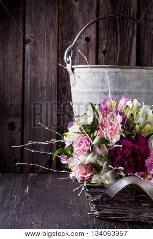 Pink bouquet from gillyflowers and white alstroemeria in the basket on old rustic wooden background with metal bucket