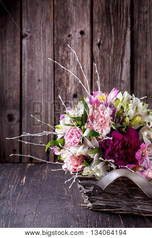 Pastel bouquet from gillyflowers and white alstroemeria in the basket on old rustic wooden background